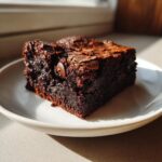 A close-up of a fudgy, dark chocolate sweet potato brownies slice with visible chocolate chips on a white plate.