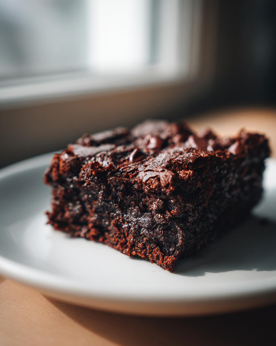 A close-up, fudgy square of sweet potato brownies topped with chocolate chips on a white plate.