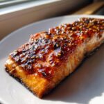 A close-up of a perfectly cooked, flaky air fryer salmon fillet with a shiny, dark honey-mustard glaze.