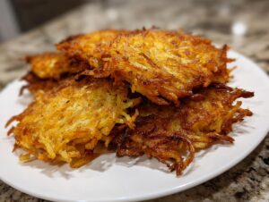 A close-up of several crispy, golden brown potato latkes stacked on a white plate.