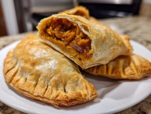 Close-up of golden baked pumpkin empanadas, one cut open to show the spiced pumpkin filling.