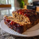 A thick slice of juicy Keto meatloaf covered in a rich, dark glaze, resting on a white plate.