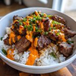 Close-up of Korean BBQ steak rice bowls featuring marinated steak pieces over white rice, drizzled with spicy orange sauce and topped with green onions.
