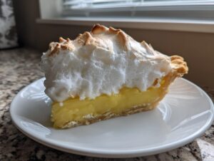 A tall slice of lemon meringue pie showing bright yellow filling and high, toasted meringue peaks.
