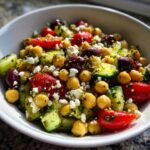 Close-up of a vibrant mediterranean chickpea salad featuring chickpeas, cucumbers, tomatoes, olives, and feta cheese.