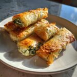 A stack of golden, flaky Mediterranean Spinach and Feta Cheese Crisps on a white plate.