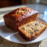 One whole and one sliced mini banana bread loaf showing chocolate chips, sitting on a white plate.