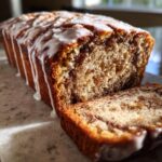 Close-up of moist apple fritter bread loaf with a thick cinnamon swirl and drizzled with white vanilla glaze.