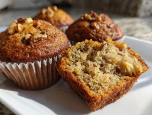 A close-up of moist banana nut muffins, one cut open showing the texture and banana pieces inside.