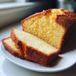 Close-up of a moist cream cheese pound cake loaf, with two thick slices cut and resting on a white plate.