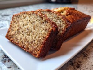 Close-up of two thick slices of moist greek yogurt banana bread on a white platter.