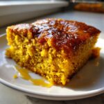 Close-up of a moist, square slice of bright orange pumpkin dump cake drizzled with a shiny glaze.