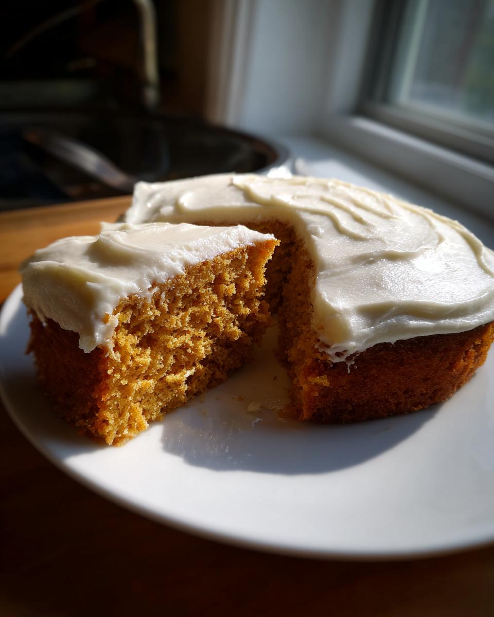 A slice removed from a homemade pumpkin poke cake topped with thick white frosting, sitting on a white plate.