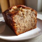 A close-up of a thick slice of moist greek yogurt banana bread with a golden-brown crust.