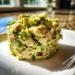 A molded serving of creamy avocado chicken salad topped with fresh dill and chunks of avocado.