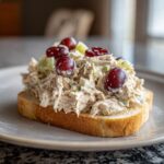Close-up of an open-faced chicken salad sandwich piled high with creamy chicken salad, grapes, and celery on toasted bread.