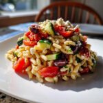 Close-up of a serving of mediterranean pasta salad featuring orzo, cherry tomatoes, cucumber, olives, and crumbled feta cheese.