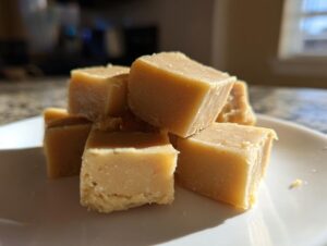 A stack of creamy, square-cut peanut butter fudge recipe pieces resting on a white plate.