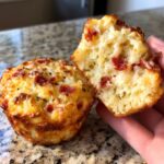 A hand holds open one of the delicious pizza muffins, showing the fluffy interior filled with cheese and pepperoni bits.