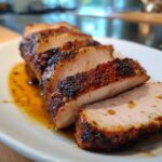Close-up of several thick slices of juicy pork loin roast showing a dark, seasoned crust and tender interior.