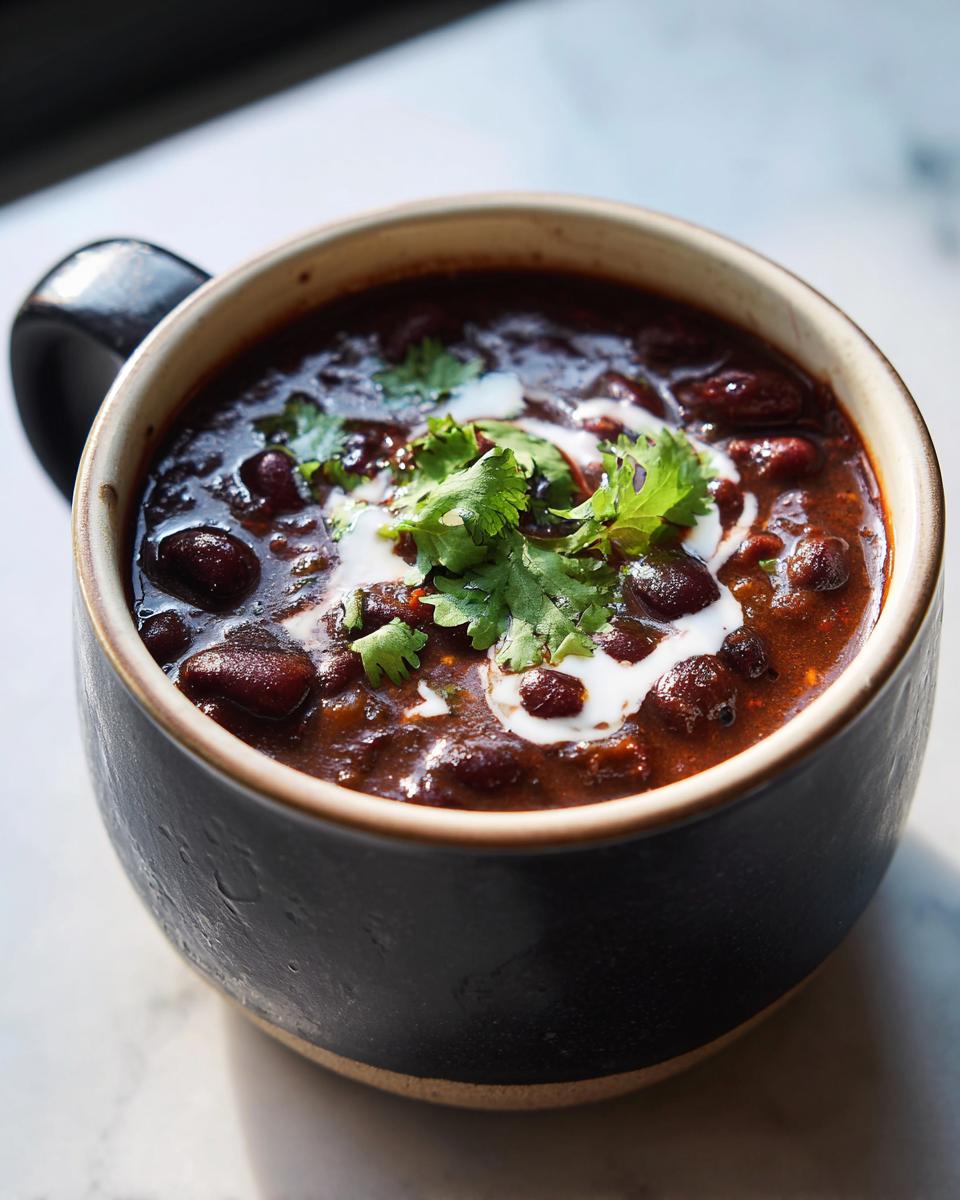 A close-up of rich, dark black bean soup topped with a swirl of cream and fresh cilantro.