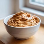 A close-up of thick, richly colored onion dip piled high in a white ceramic bowl.