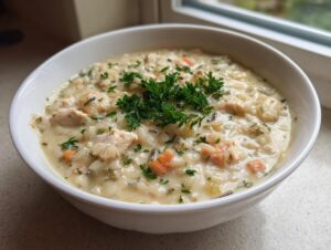 A close-up of a creamy, savory rice soup with chunks of chicken, carrots, and wild rice, garnished with fresh parsley.