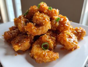 A close-up of crispy, saucy Bang Bang Shrimp piled high and garnished with sesame seeds and green onions.