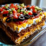 A cross-section view of a rich Seven layer dip showing layers of meat, cheese, sour cream, salsa, and fresh toppings.