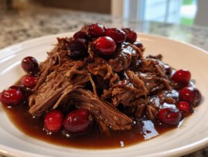 A serving of tender, shredded cranberry pot roast topped with glossy whole cranberries in a rich sauce.