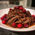 A serving of tender, shredded cranberry pot roast covered in rich sauce and garnished with fresh cranberries.