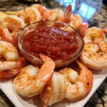 A platter of cooked shrimp arranged around a small glass bowl of zesty red shrimp cocktail sauce.
