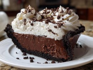A decadent slice of Christmas chocolate cream pie featuring a dark crust, rich chocolate filling, and high peaks of whipped cream topped with chocolate shavings.