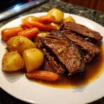 Plate of tender, shredded slow cooker pot roast served with baby potatoes and carrots in rich gravy.