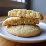 Close-up of three soft sugar cookies stacked on a white plate, showing the crumb texture of the broken top cookies.