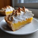 Close-up of a slice of lemon meringue tart showing bright yellow filling and perfectly toasted, peaked meringue.