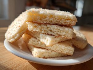 Close-up of thick, pale sugar cookies cut into squares and stacked on a white plate, showing texture.