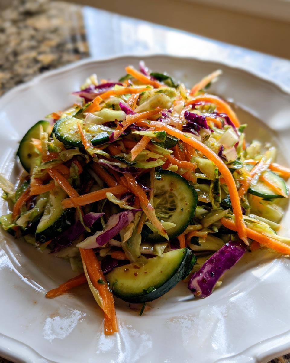A close-up of a vibrant cabbage salad featuring shredded carrots, cucumber slices, and purple cabbage.