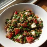 Close-up of a vibrant lentil salad mixed with diced tomatoes, feta cheese, and fresh parsley.