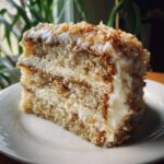 A close-up slice of white German chocolate cake layered with creamy frosting and toasted coconut flakes.
