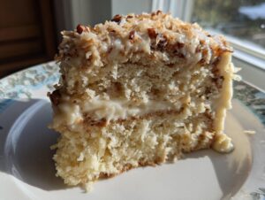 Close-up of a moist slice of white German chocolate cake showing layers and coconut pecan frosting.