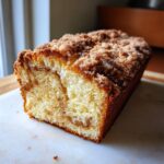 A close-up, appetizing view of a freshly baked coffee cake loaf with a thick cinnamon streusel topping.