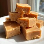 A stack of perfectly cut, light brown maple fudge squares resting on a white plate.