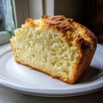 A thick slice of homemade soda bread showing its light, fluffy interior and golden-brown crust, resting on a white plate.