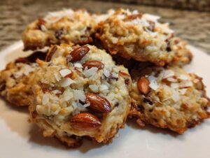 A pile of freshly baked almond joy cookies topped with whole almonds and shredded coconut.