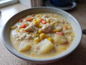 Close-up of a creamy bowl of chicken corn chowder filled with potatoes, corn, carrots, and shredded chicken.
