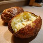 Close-up of a perfectly cooked air fryer baked potato, split open to show fluffy interior seasoned with spices.