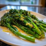 Close-up of bright green, tender broccolini spears tossed with garlic and lemon zest on a white plate.
