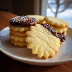 Close-up of star-shaped butter cookies, some stacked and dipped in chocolate with colorful sprinkles.