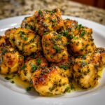 A pile of golden brown, glistening chicken bites tossed in a garlic butter sauce and topped with fresh parsley.